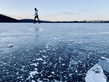 Woman walking on frozen lake against sky during winter