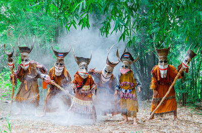 People wearing traditional clothing standing on land in forest