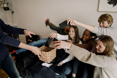 Teenage girls and boys keeping mobile phones in basket at home