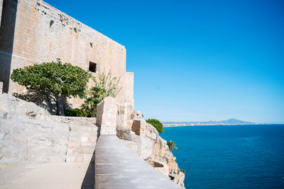 Stone wall by sea against clear blue sky