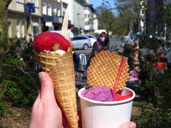 Cropped image of hands holding ice cream against buildings in city