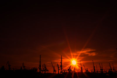 Silhouette cranes against sky during sunset