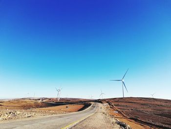 Road passing through land against clear blue sky