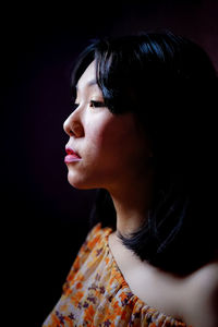 Close-up of woman looking away against black background