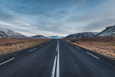 Empty road leading towards mountains against sky