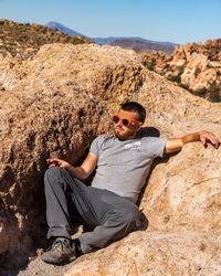 Full length of man sitting on rock during sunny day