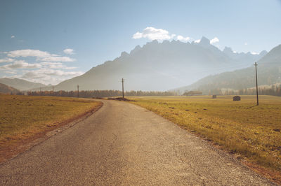 Empty road amidst field against sky