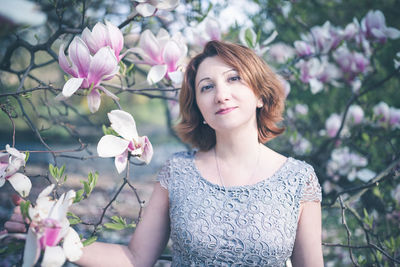 Cheerful middle aged armenian woman in an elegant dress under the magnolia blooming tree. spring pa