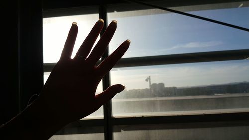 Close-up of hand touching window against sky