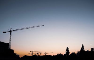 Low angle view of silhouette cranes against sky during sunset