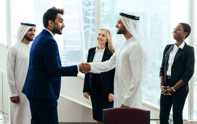 Smiling colleagues looking at businessmen shaking hands in meeting at office