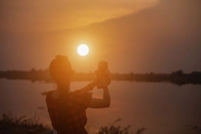 Side view of silhouette woman standing on shore against sunset sky