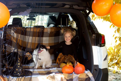 Portrait of cute girl sitting with dog in car trunk