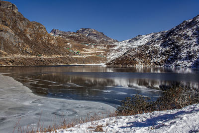 Scenic view of frozen lake by mountains against clear sky