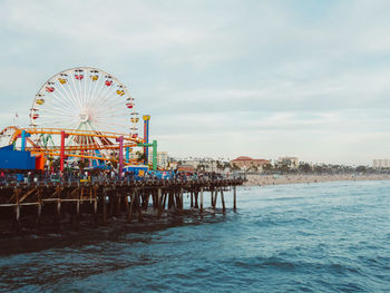 Ferris wheel in city by sea against sky