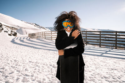 African american woman with goggles and a snowboard on a snowy mountain during winter