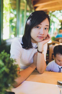 Portrait of young woman sitting on table. her little boy sitting next to her.  