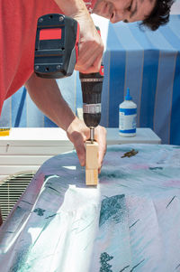 Man using a drill to build a piece of furniture on a rooftop.