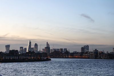 Cityscape by thames river against sky