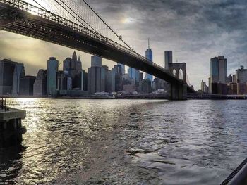 Bridge over river by buildings in city against sky