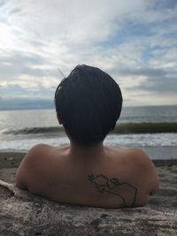 Rear view of shirtless man sitting on beach
