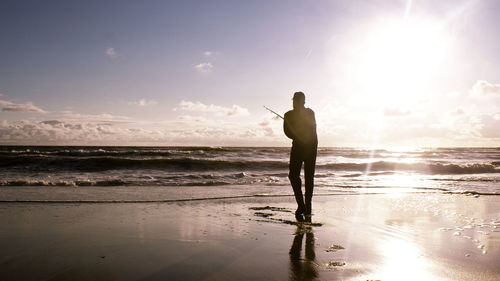 Rear view of silhouette man standing at beach during sunset