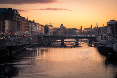 Bridge over river against buildings in city during sunset