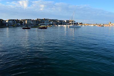 Sailboats moored in sea against sky in city