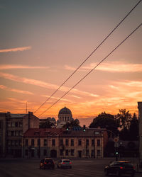 Cars on street by buildings against sky during sunset