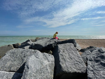 Man sitting on rock looking at sea against sky