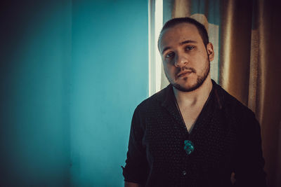 Portrait of young man standing against wall at home