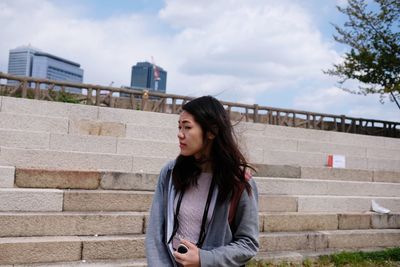 Young woman standing on staircase against sky