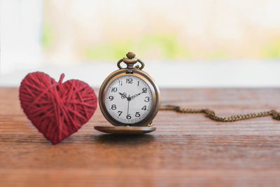 Close-up of pocket watch with heart shape wool on table