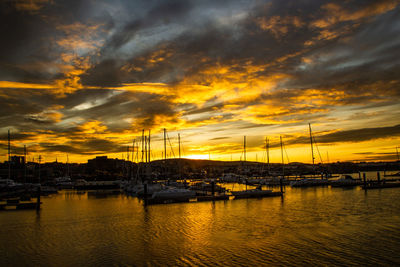 Sailboats moored at harbor during sunset