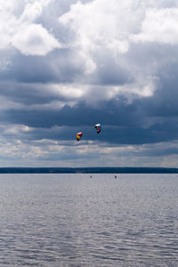 Distant view of people kiteboarding over sea against sky