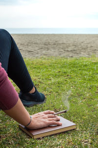 Low section of man on grass by sea against sky