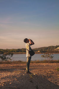 Man screaming while standing on lakeshore against sky during sunset