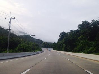 Road by trees against sky