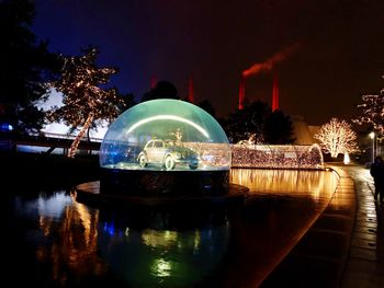 Illuminated built structure by lake against sky at night