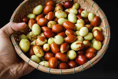 Cropped hand holding fruits in basket against black background