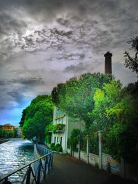 View of trees by river against cloudy sky