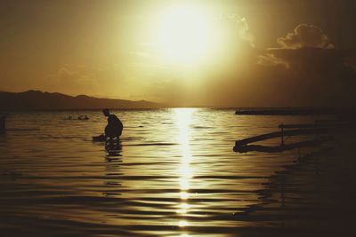 Side view of silhouette woman releasing paper boat on sea at sunset