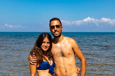 Portrait of smiling young couple on beach against sky in castelsardo