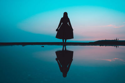 Rear view of silhouette person standing by swimming pool against sky