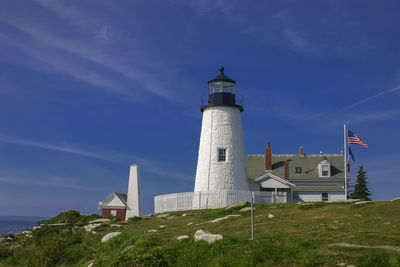 Low angle view of pemaquid point light and american flag against blue sky