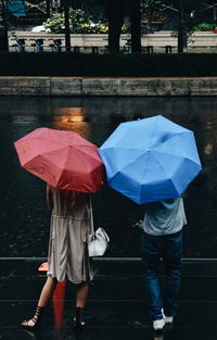 Rear view of man and woman with umbrella standing on street during rainy season