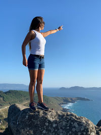 Full length rear view of woman standing on rock against sky