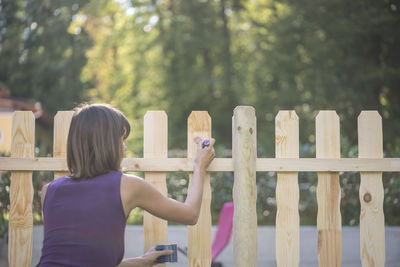 Rear view of woman standing by railing against fence