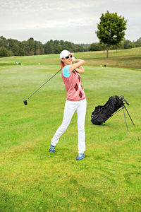 Full length of mature woman playing golf on grassy field against cloudy sky