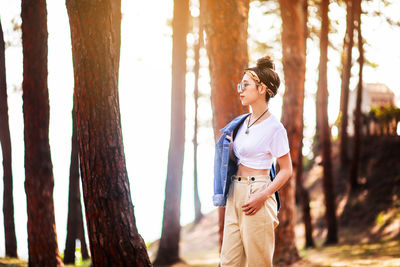 Woman standing by tree trunk in forest